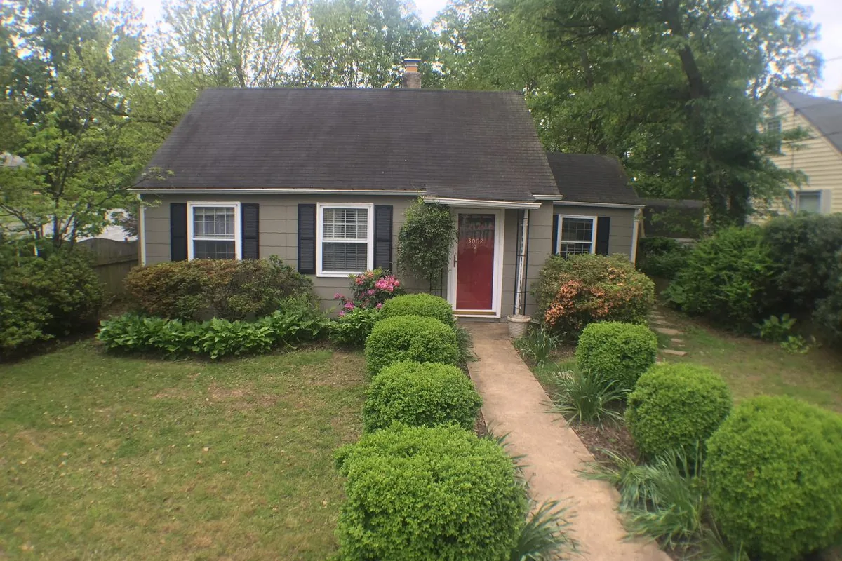 Brick Cape Cod single-family rental home with a red door, manicured shrubs, and a front walkway on a tree-lined Maryland suburban street