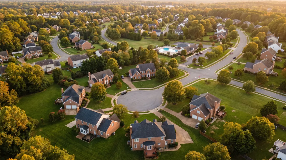 Aerial view of an established West End / Short Pump neighborhood in Henrico County, Richmond, Virginia with brick colonial homes, curving tree-lined streets, and a dense mature canopy at golden hour